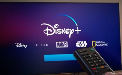 shot of the Disney+ loading screen on a TV with a person holding a remote in front
