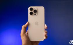 shot of a hand holding the Apple iPhone 16 Pro Mac in front of a dark blue gradient background