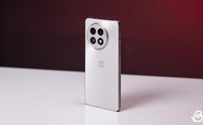 shot of the OnePlus 13R placed upright on a white desk with red gradient background focussing on the phone's rear panel