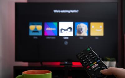 hand holding remote in front of a TV with a preview of Netflix profiles screen