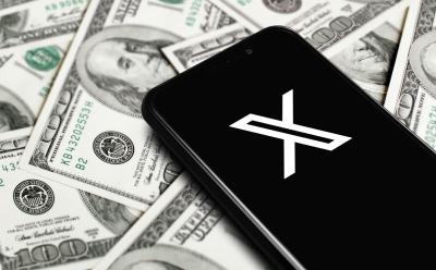 X app logo on a phone that's placed on a pile of US dollars